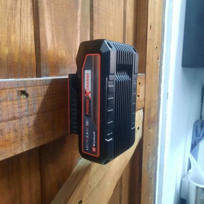 A black and red Li-ion battery charger or battery pack mounted on a wooden door, with a white wall and household items visible on the right side.