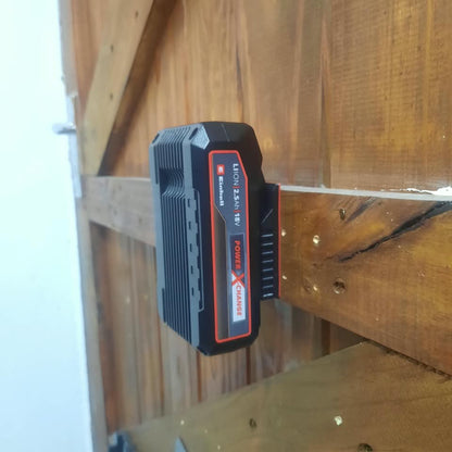 A black cordless tool battery with red and white labeling, photographed resting on a wooden surface in a real indoor setting.