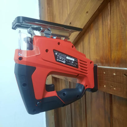 A cordless jigsaw with a red and black body, mounted on a wooden wall next to a white wall.