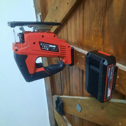 A cordless jigsaw with a red and black body is shown mounted against a wooden wall, with its battery pack attached. The background consists of a wooden door and a white wall.