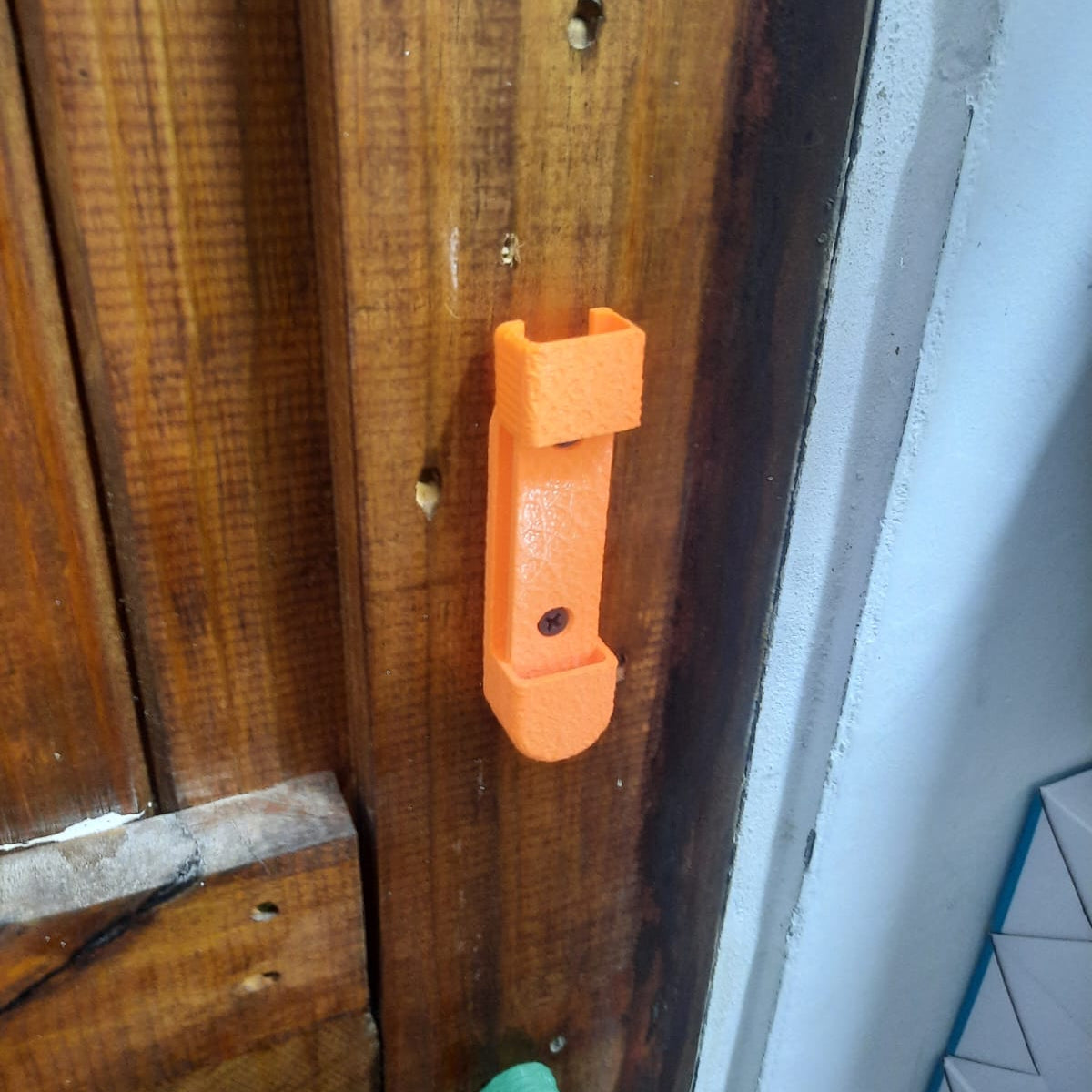 Orange tool attached to a wooden surface with a white wall in the background