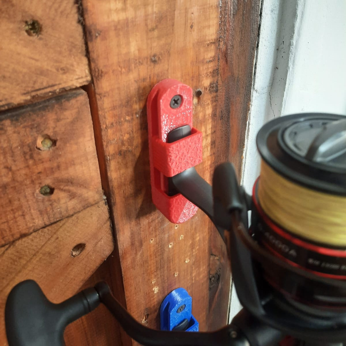 Red tool attached to a wooden surface with fishing reel in the foreground