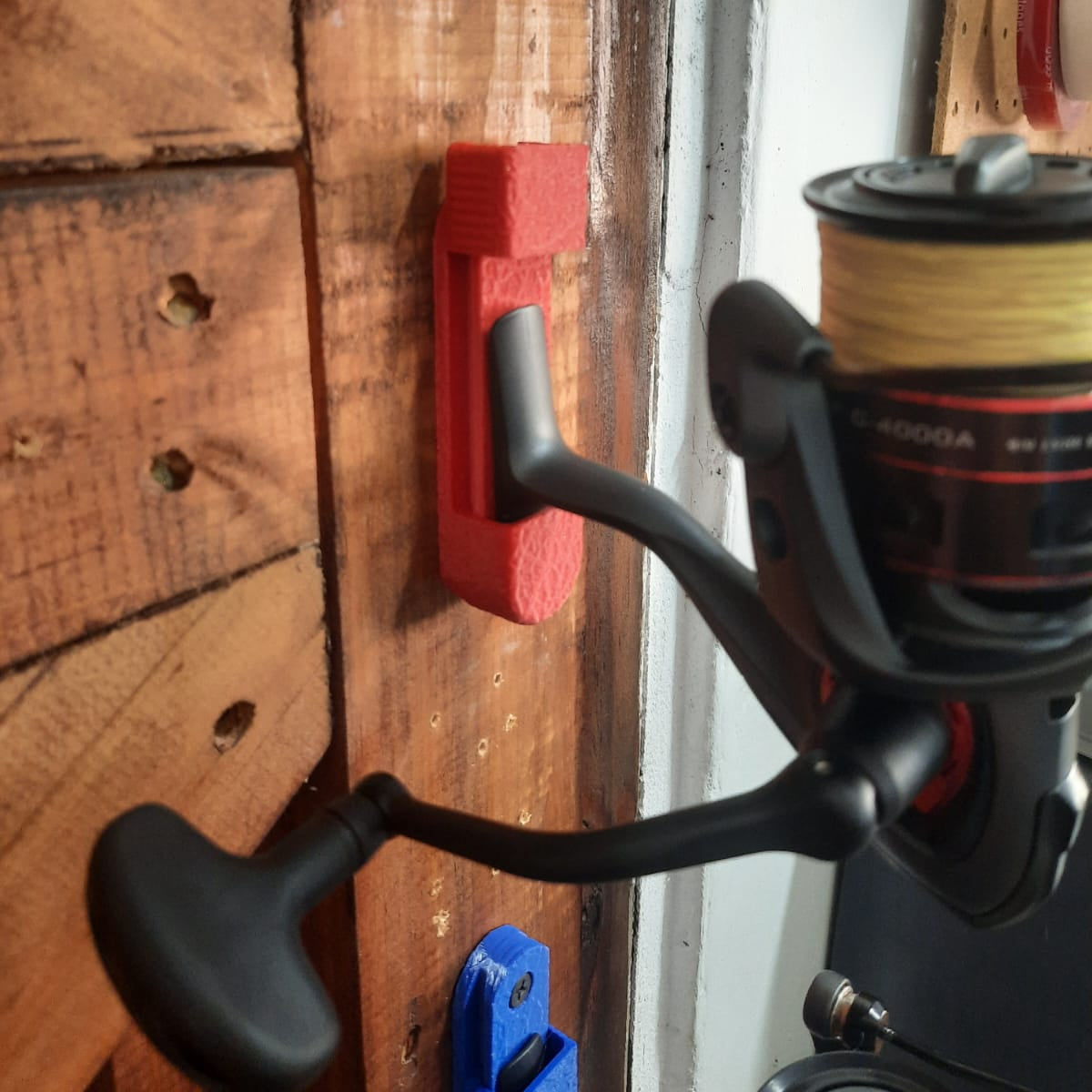 Fishing reel attached to a wooden surface with a red tool mount
