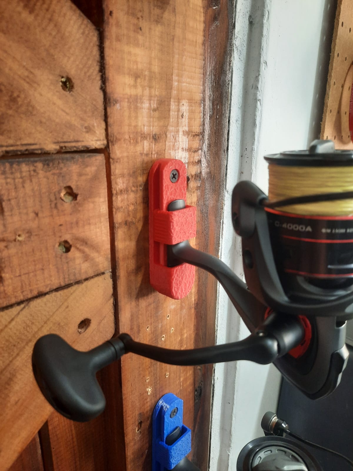 Fishing reel attached to a wooden surface with a red tool holder.
