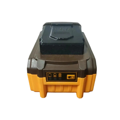 A cordless tool battery pack with a black top cover and yellow-and-brown body, resting on a dark reflective surface against a plain light wall.